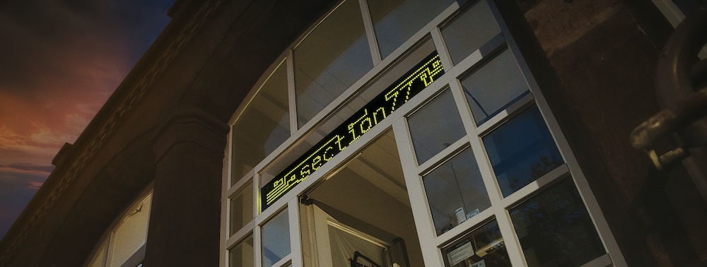 FlipDot Display mit dem Text "Section77" über einer Eingangstür